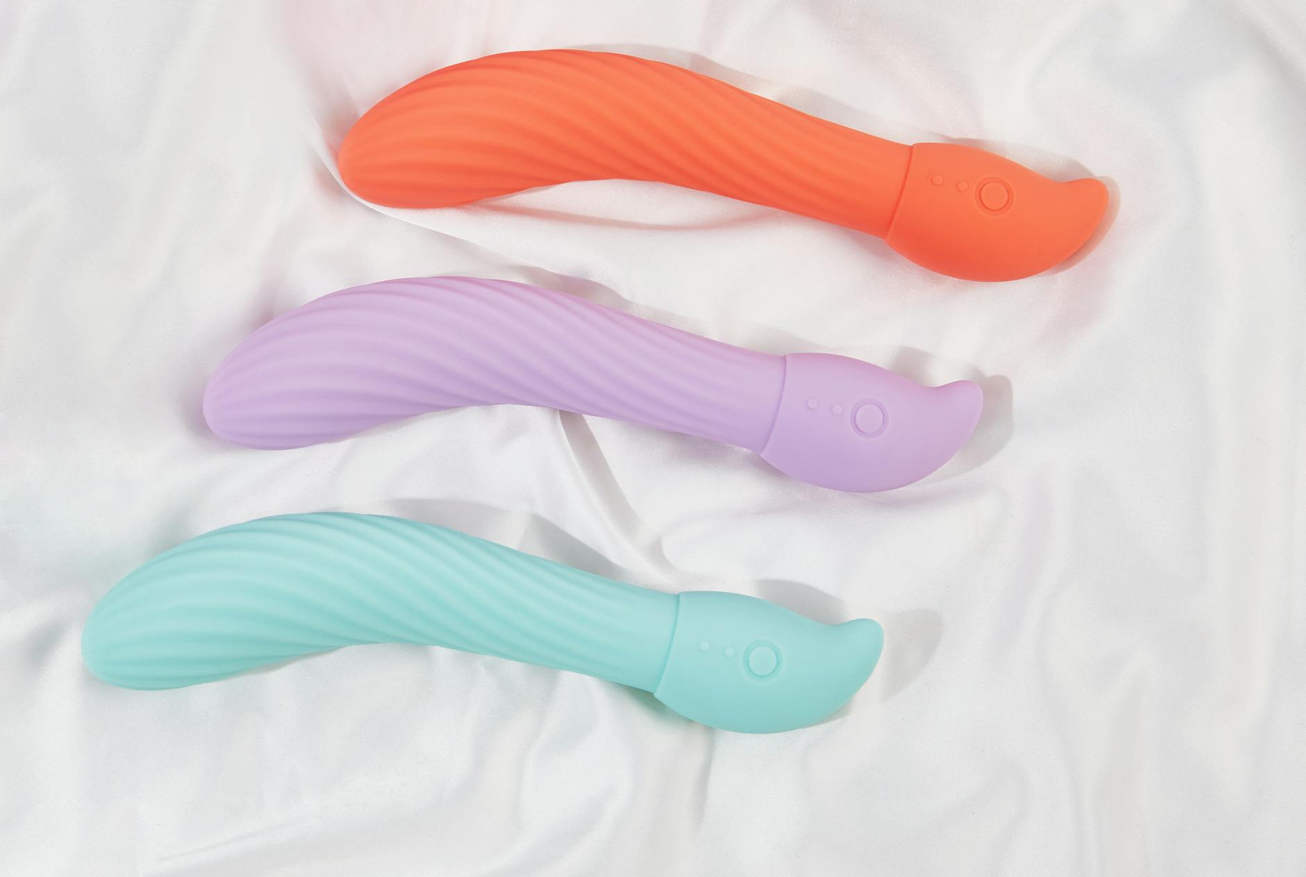 Three colorful clitoral vibrators arranged on white fabric, highlighting their smooth design.