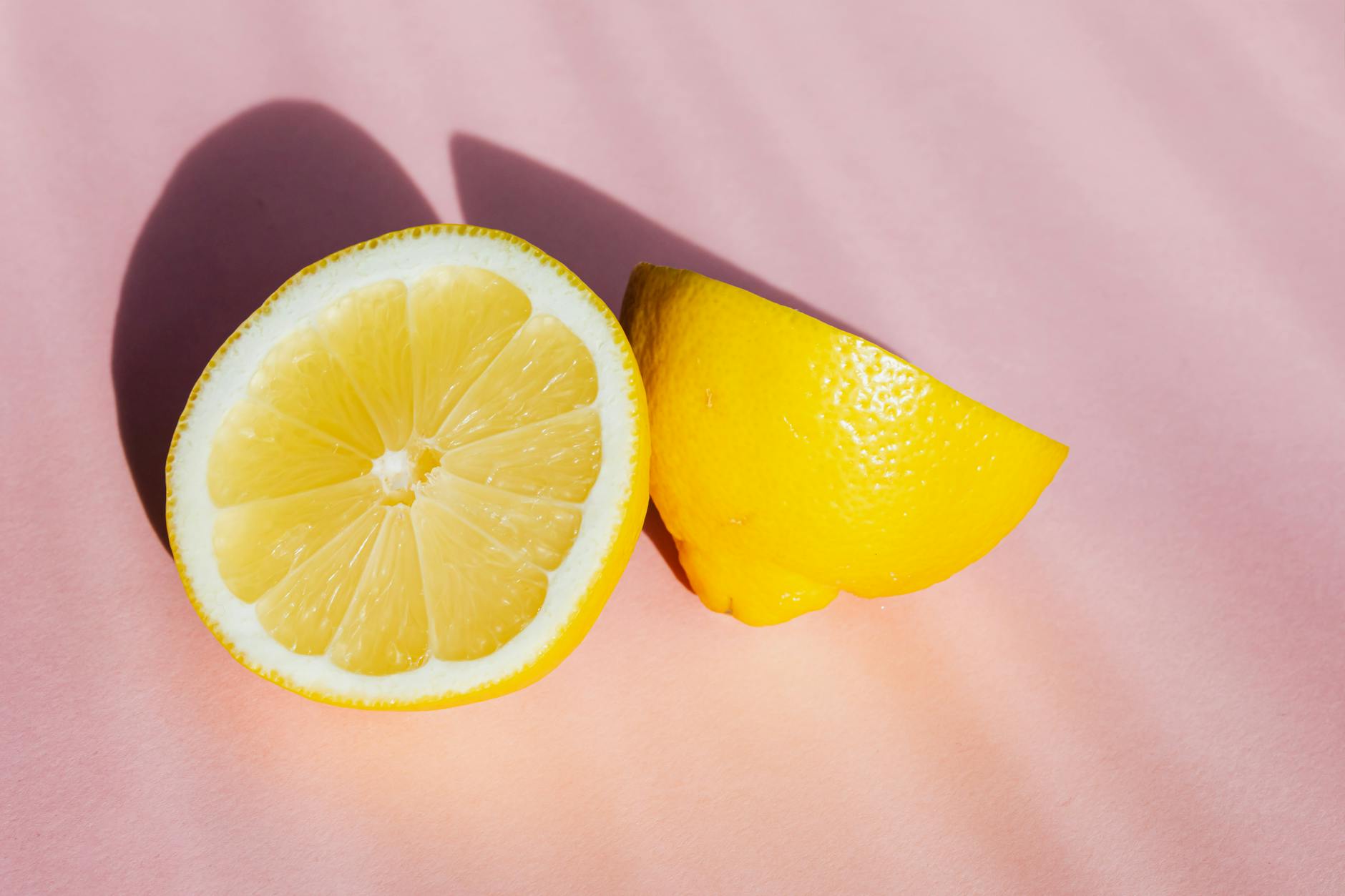 Mitades de limones frescos y jugosos sobre un fondo rosa brillante con rayos de sol