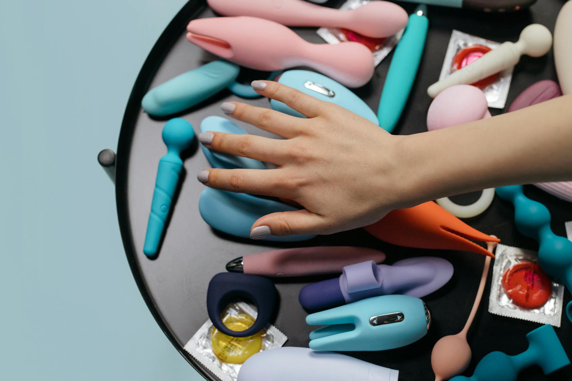 A hand reaching over a collection of colorful vibrators on a table
