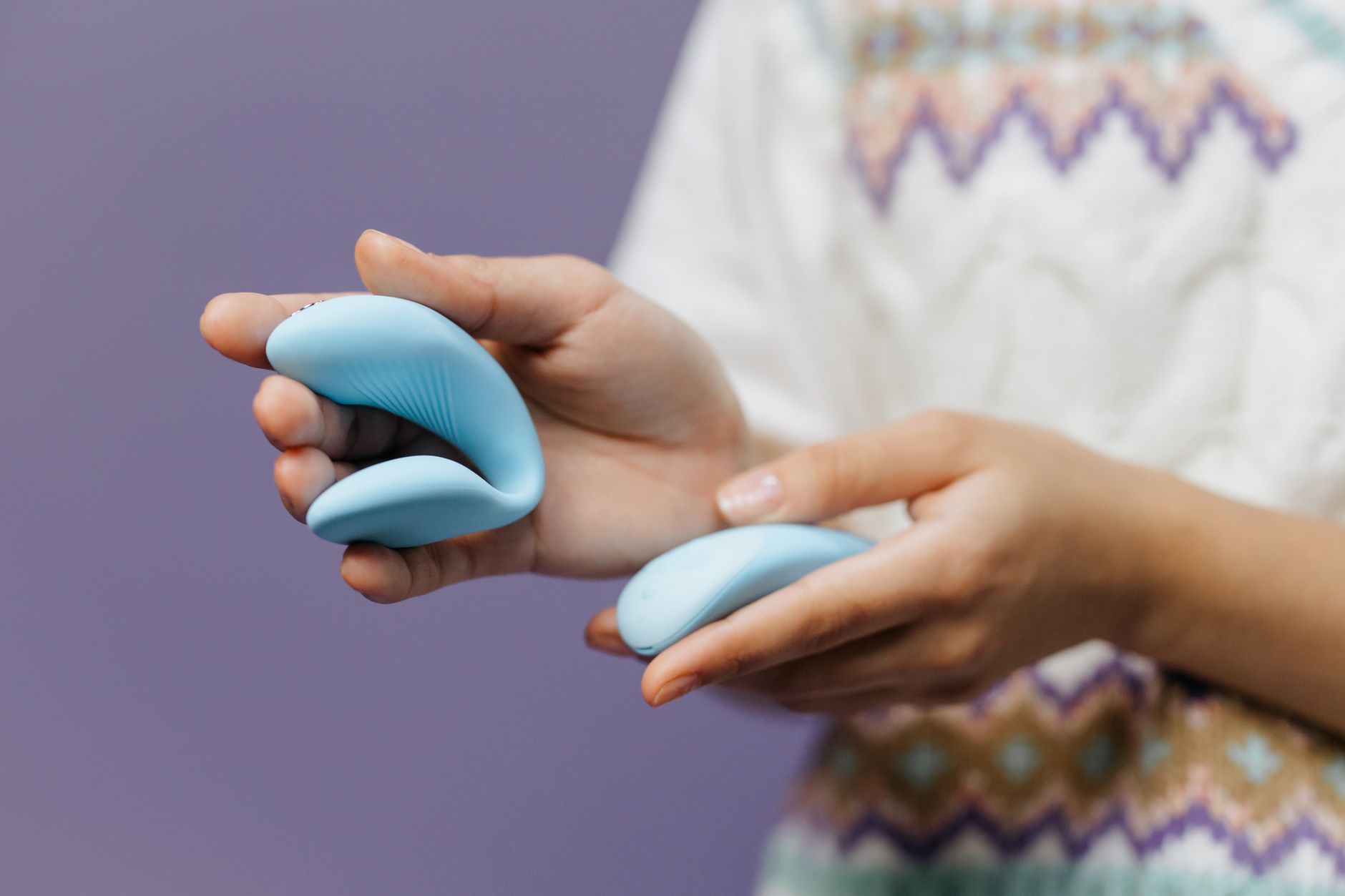 Person holding a sleek blue vibrator against a purple background, representing self-care and personal intimacy.