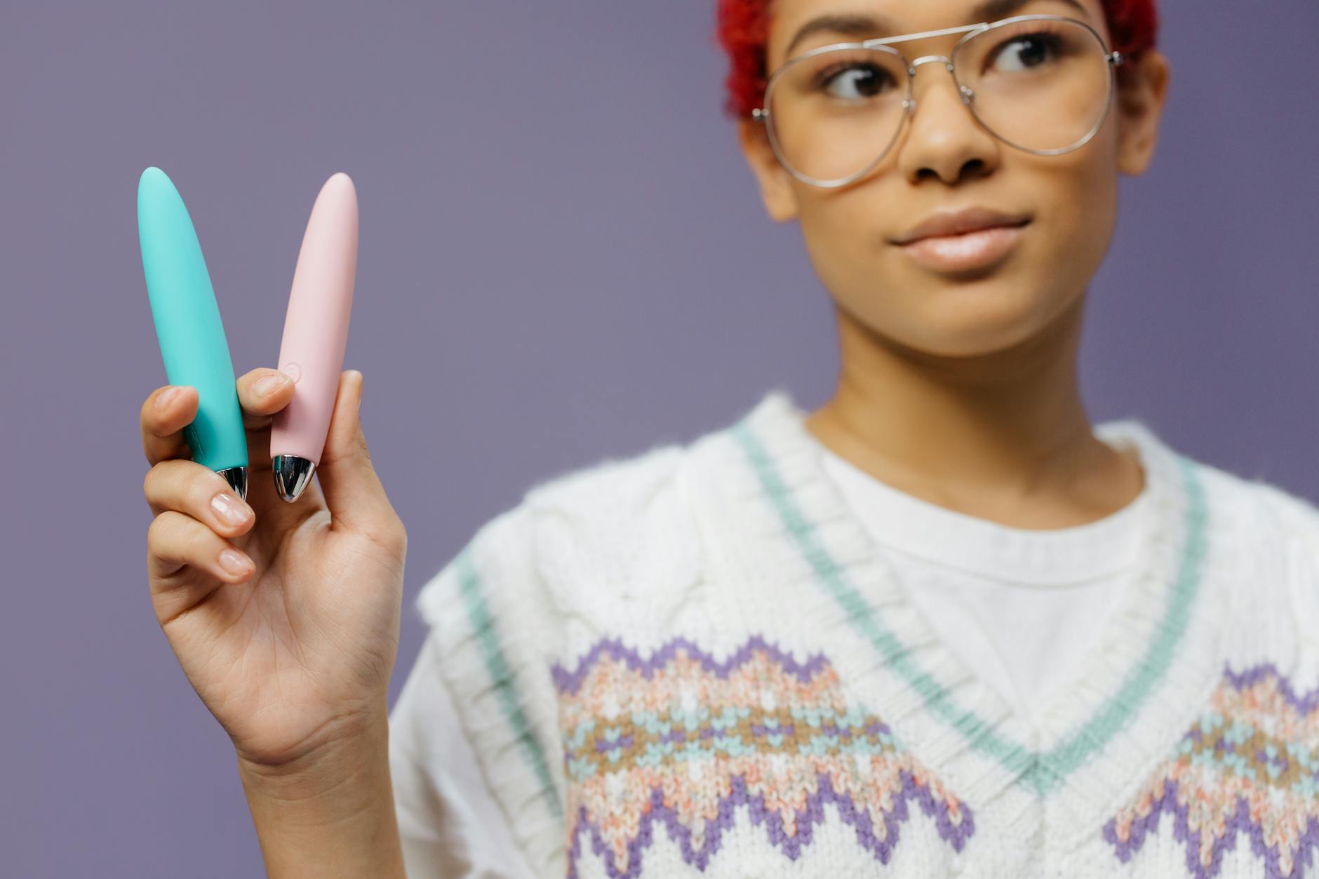 Woman holding colorful vibrators against a purple background, representing pleasure and choice